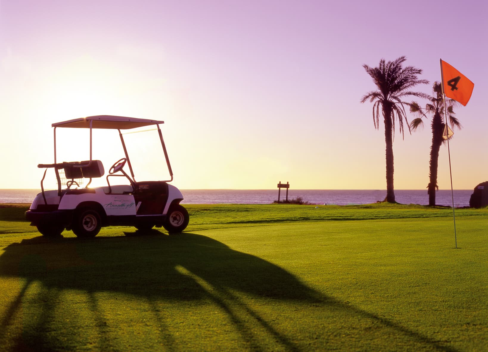 Golf buggy beside an oceanside green at Amarilla Golf, Tenerife, at sunset