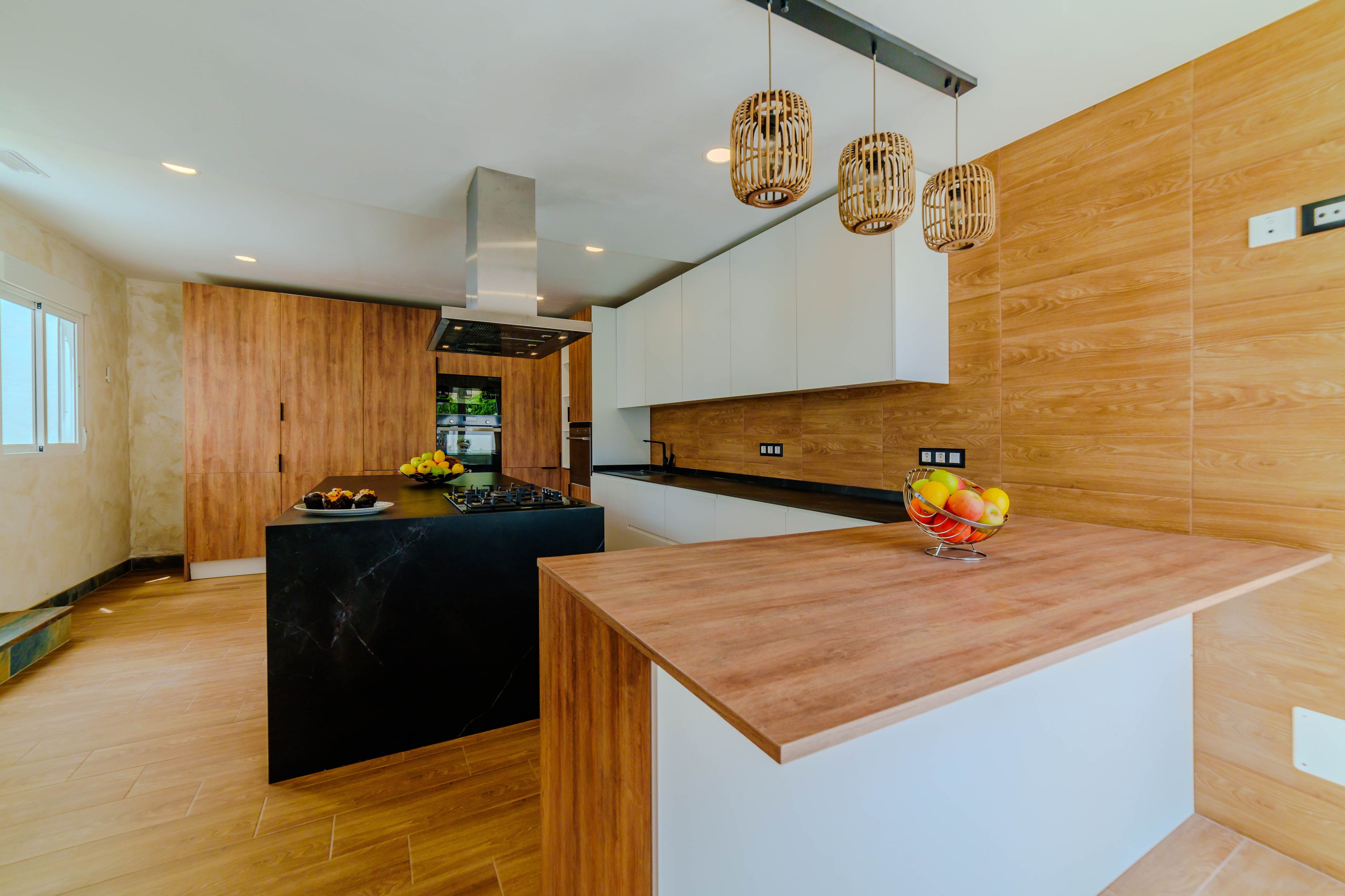 Cocina abierta con isla de piedra negra, placa de gas, campana y barra de desayuno de madera