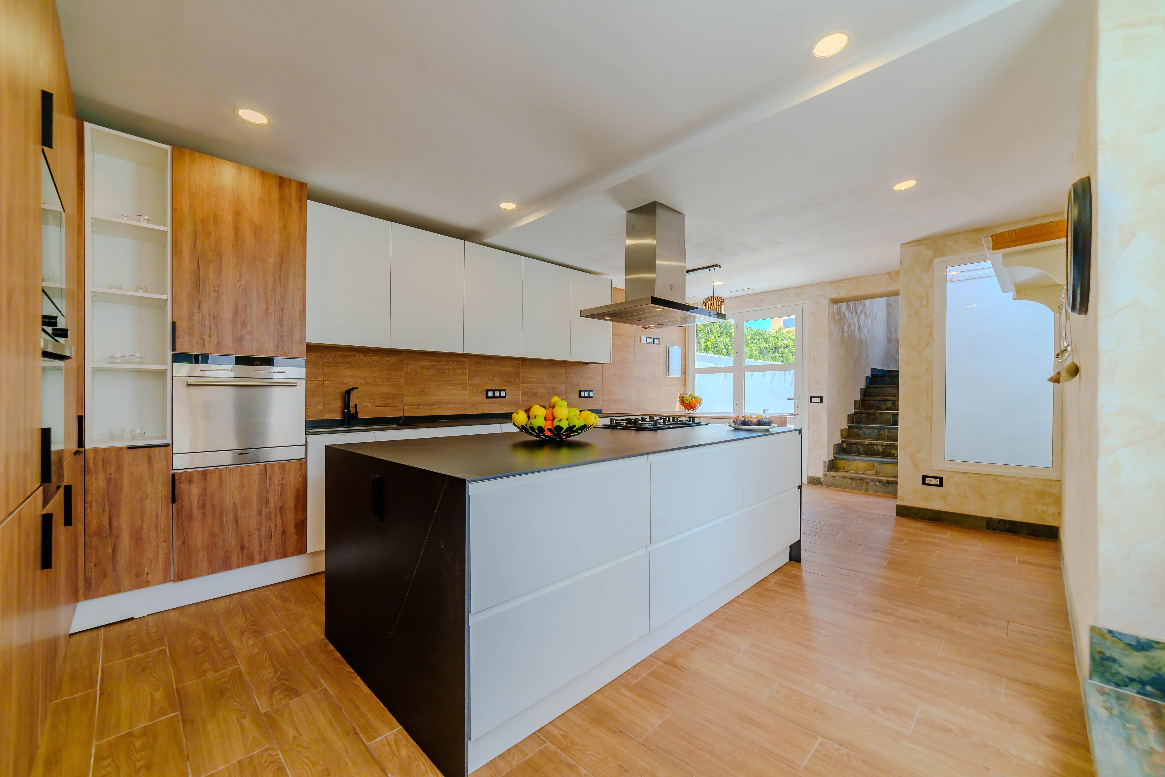 Cocina abierta con isla de piedra negra, placa de gas, campana y barra de desayuno de madera